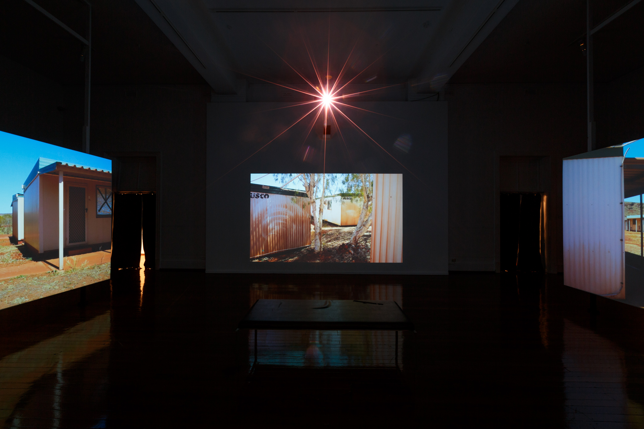 Melbourne-based artist Claire Robertson’s cinematic installation depicts an uninhabited temporary mining camp in the Pilbara, showing scenes of empty industrial villages set against the Australian outback. The installation is accompanied by a haunting original soundtrack by composer Tilman Robinson.