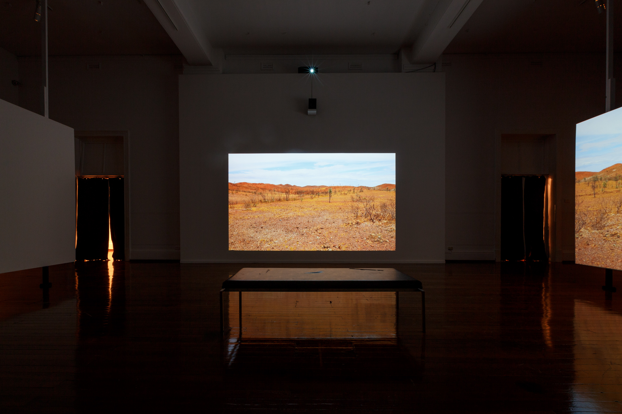 Melbourne-based artist Claire Robertson’s cinematic installation depicts an uninhabited temporary mining camp in the Pilbara, showing scenes of empty industrial villages set against the Australian outback. The installation is accompanied by a haunting original soundtrack by composer Tilman Robinson.