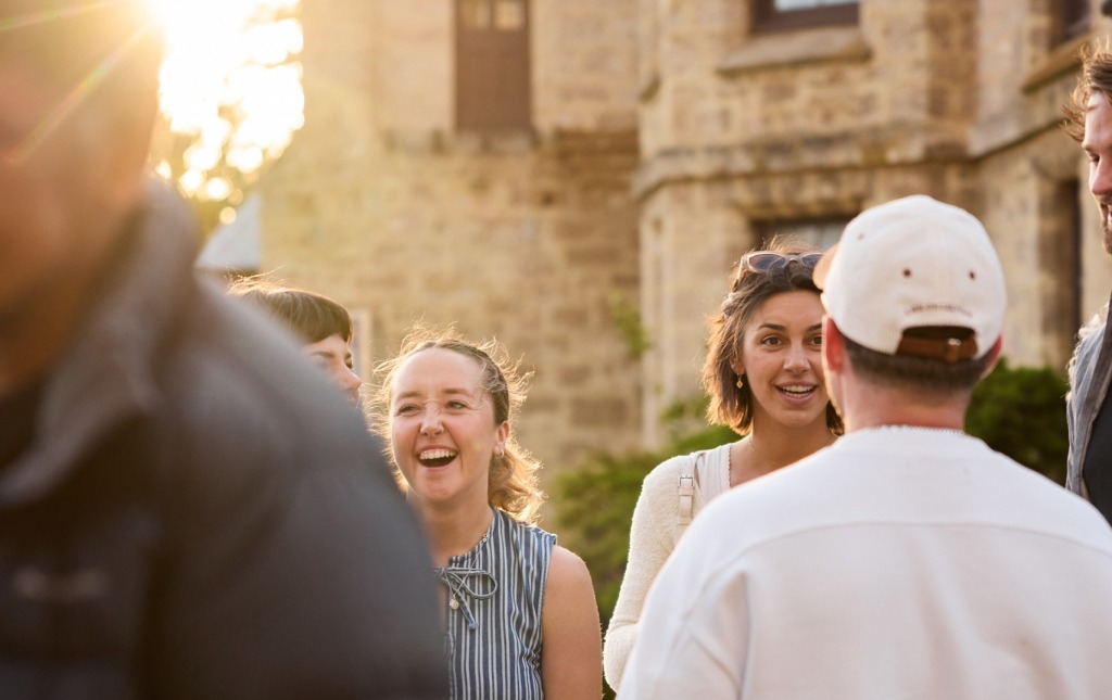 A group of people laugh and talk outside a heritage building at the Fremantle Arts Centre.